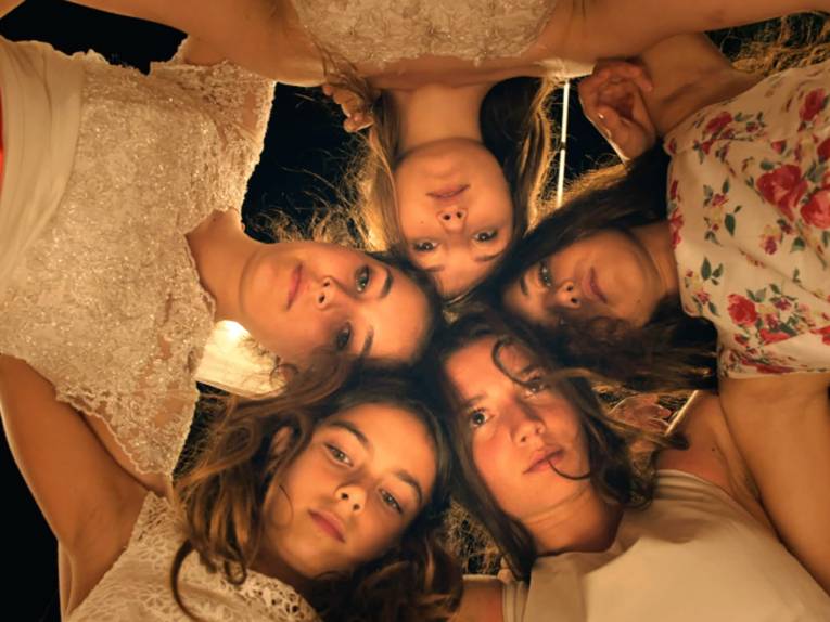 Zu sehen sind fünf Mädchen, die sich über die Kamera beugen.